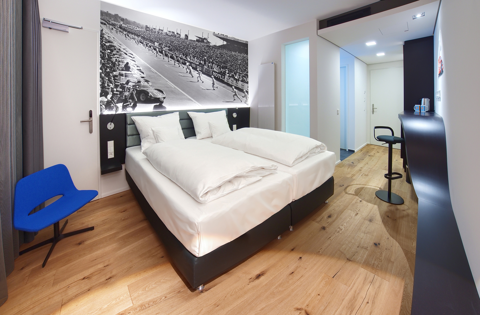 Modernes Schlafzimmer mit gemütlichem Doppelbett unter einem schwarz-weiß Bild von einem Autorennen
