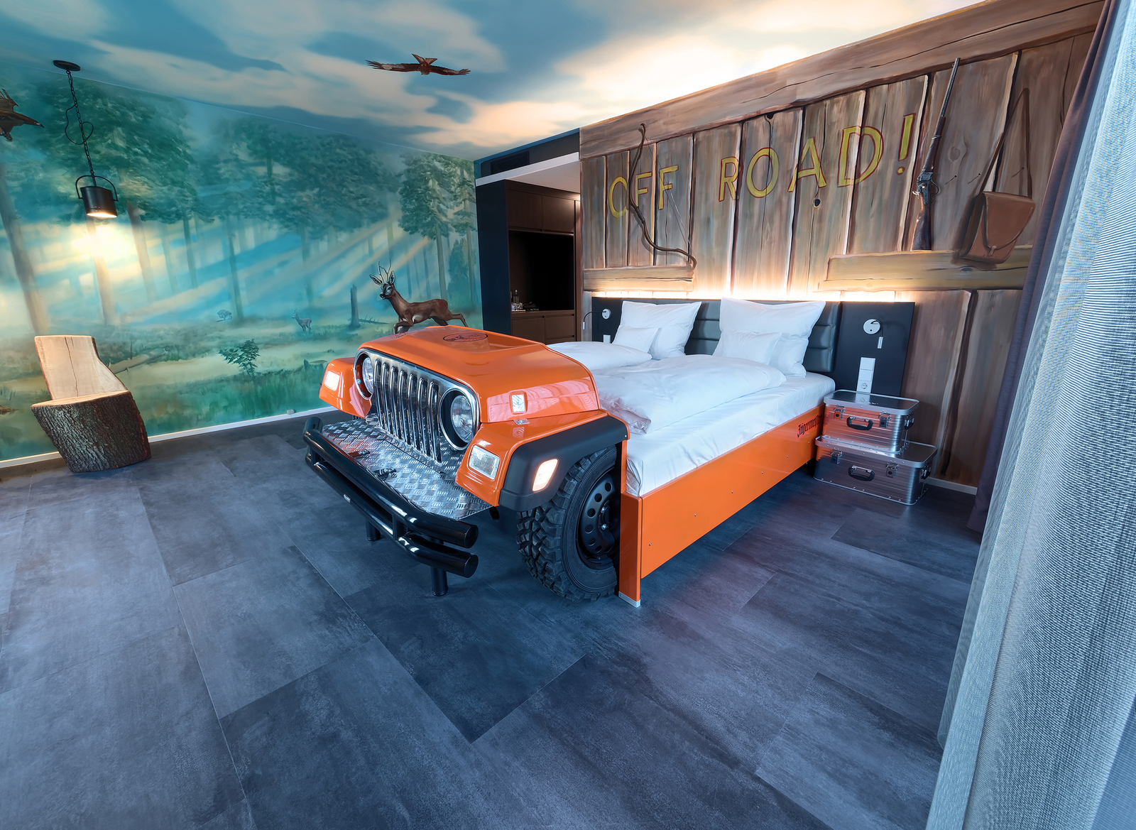 Orangefarbenes Autobett im Offroad-Themenzimmer im V8 Hotel mit bemalten Wänden im Holz- und Walddesign
