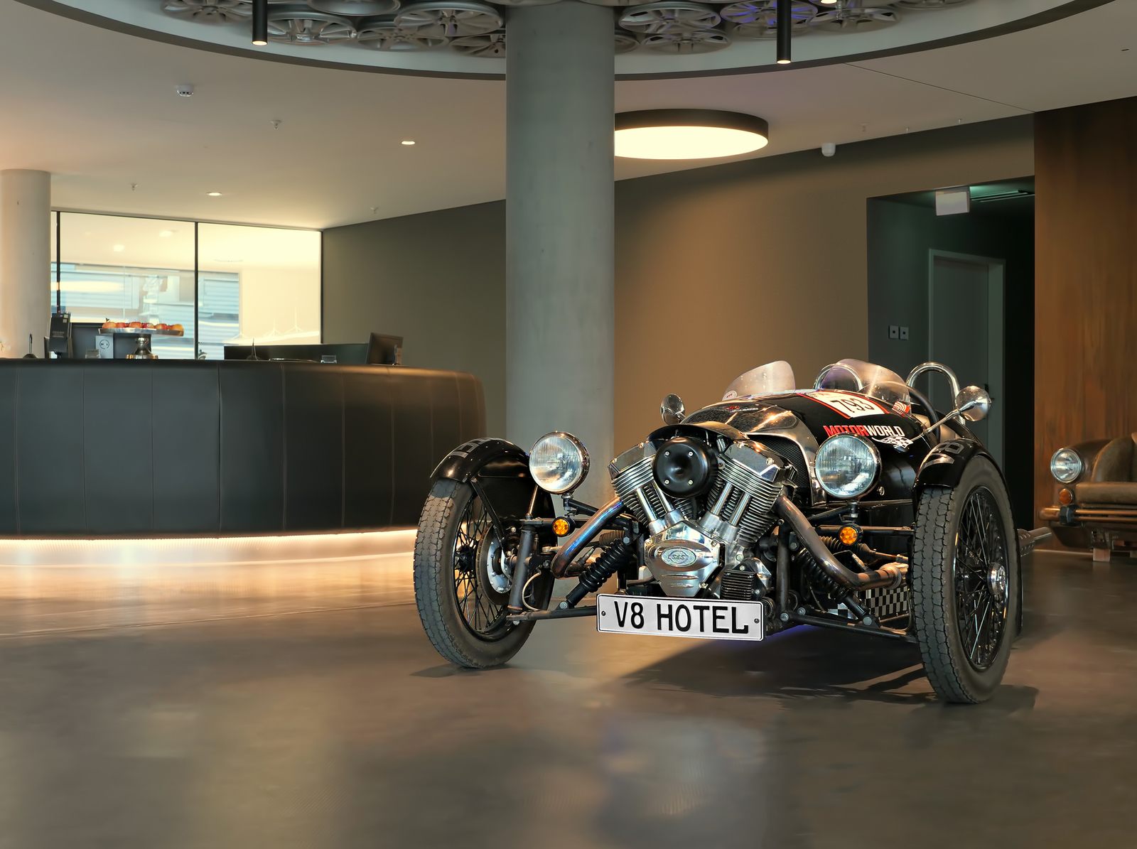 Ein schwarzes, altes Motorrad steht im Eingangsbereich des Hotels mit Kennzeichen "V8 Hotel".