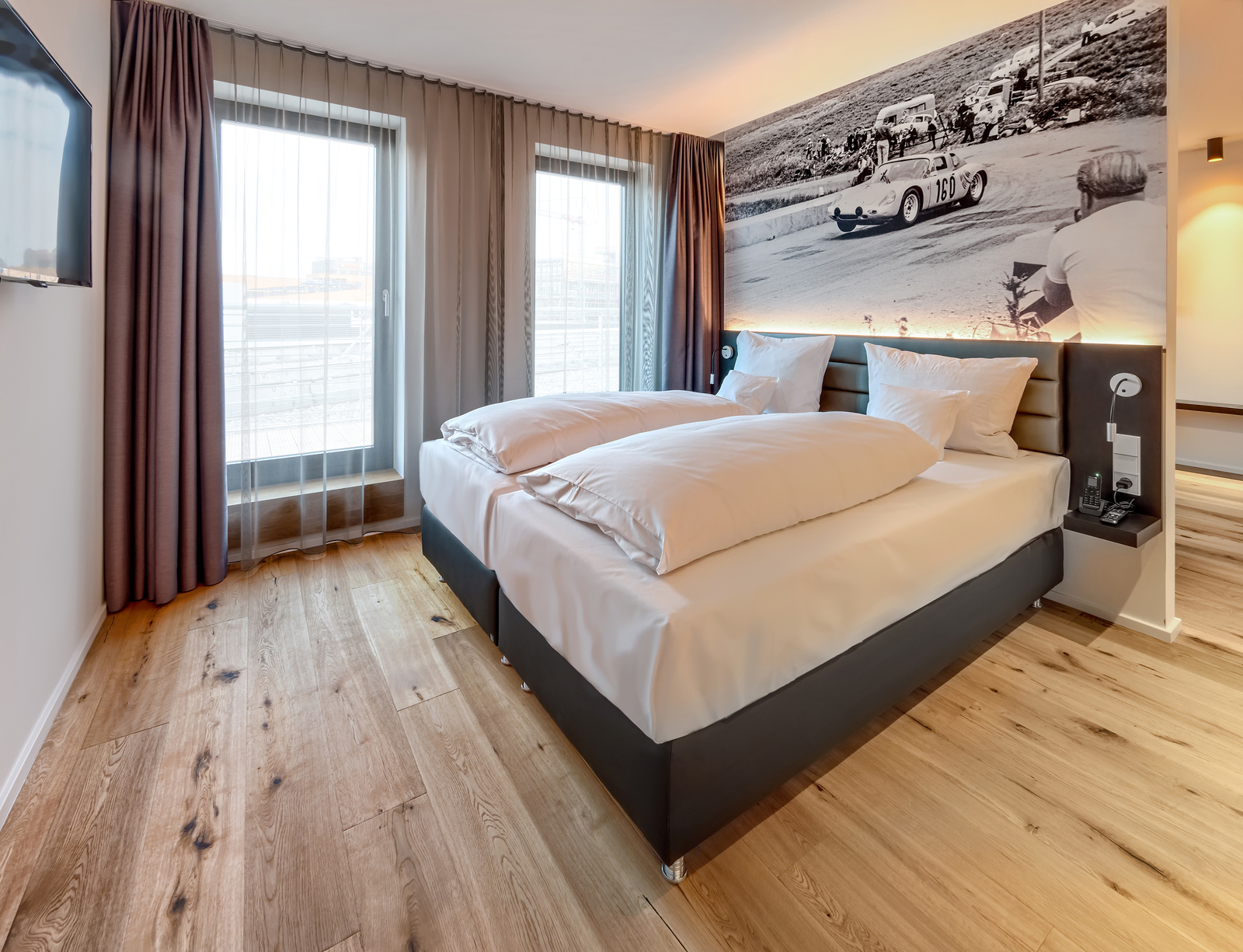 Eines der Serviced Apartments in Böblingen mit gemütlichem Doppelbett, beleuchteter Kopfleiste, großen Fenstern und TV.
