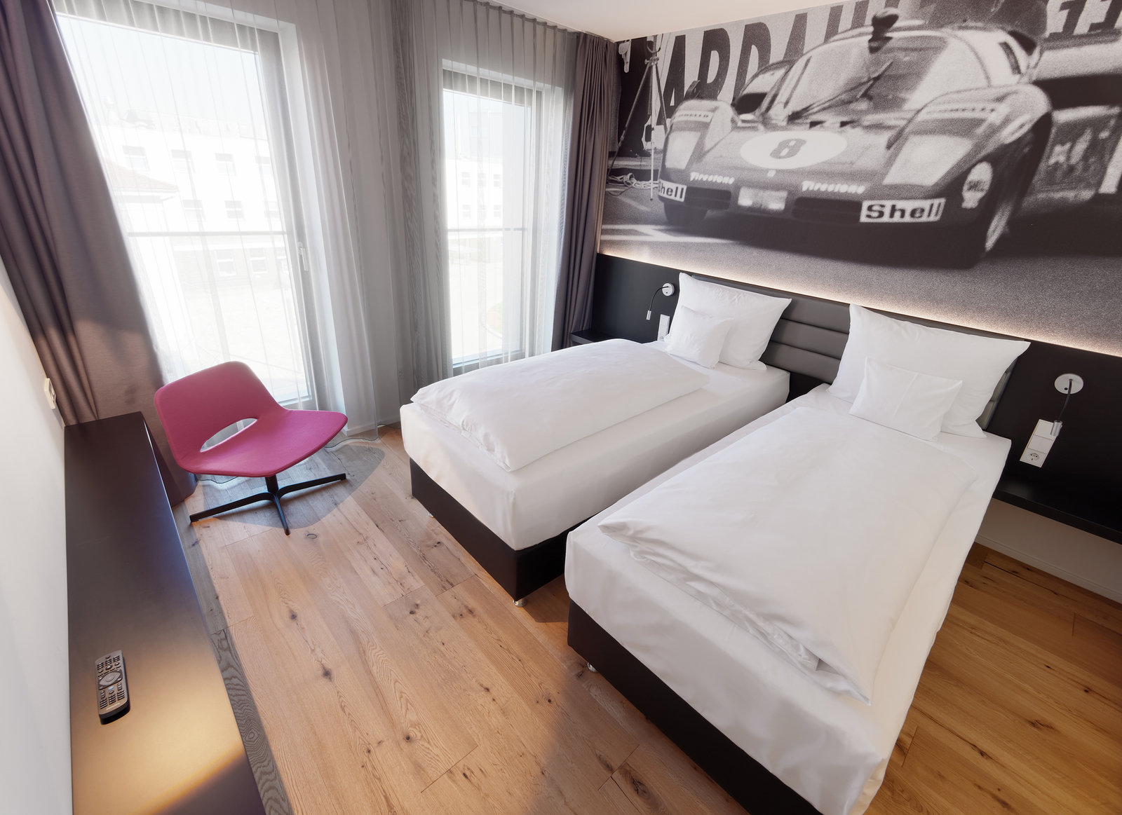 Zwei Einzelbetten unter einem schwarz-weiß Bild eines alten Rennautos im Familienhotel Stuttgart.