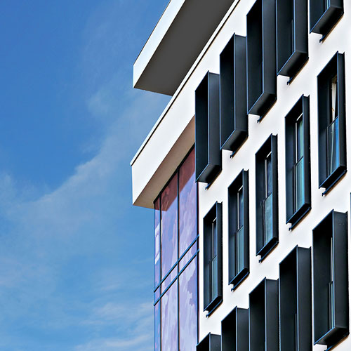 Fensterfront des V8 Themenhotels Stuttgart vor blauem Himmel.