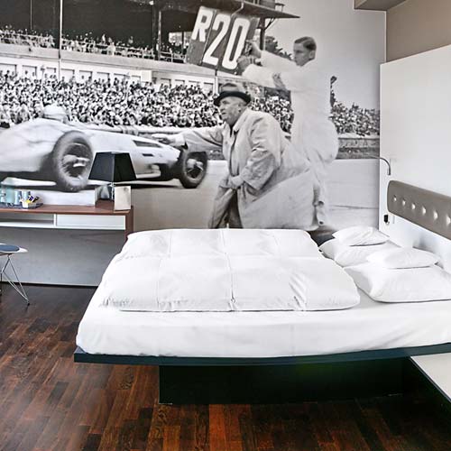 Doppelzimmer Classic mit Rennstrecken-Fototapete und gemachtem Bett im V8 Hotel Böblingen. 