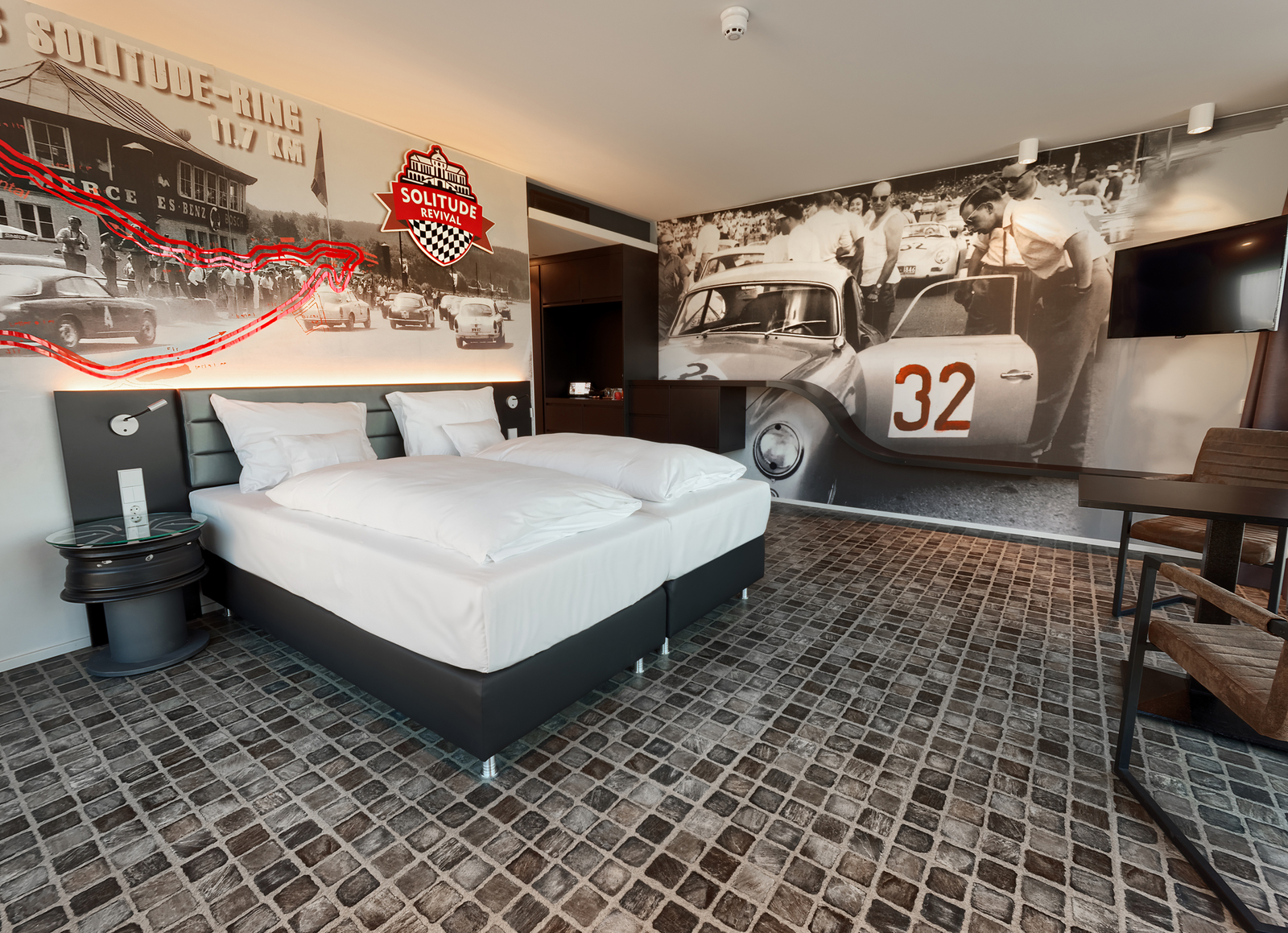 Großzügiges Solitude-Ring-Themenzimmer im V8 Hotel, dekoriert mit schwarz-weiß Motivtapeten, die die Oldtimer beim Rennen zeigen