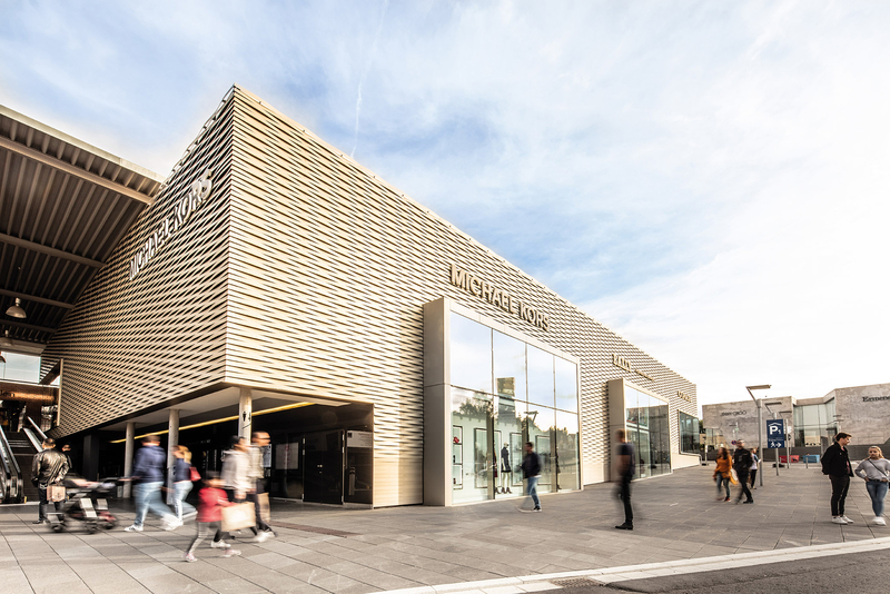 Außenansicht des Michael Kors Gebäudes im Outletcity Metzingen mit mehreren Personen, die dort shoppen gehen.