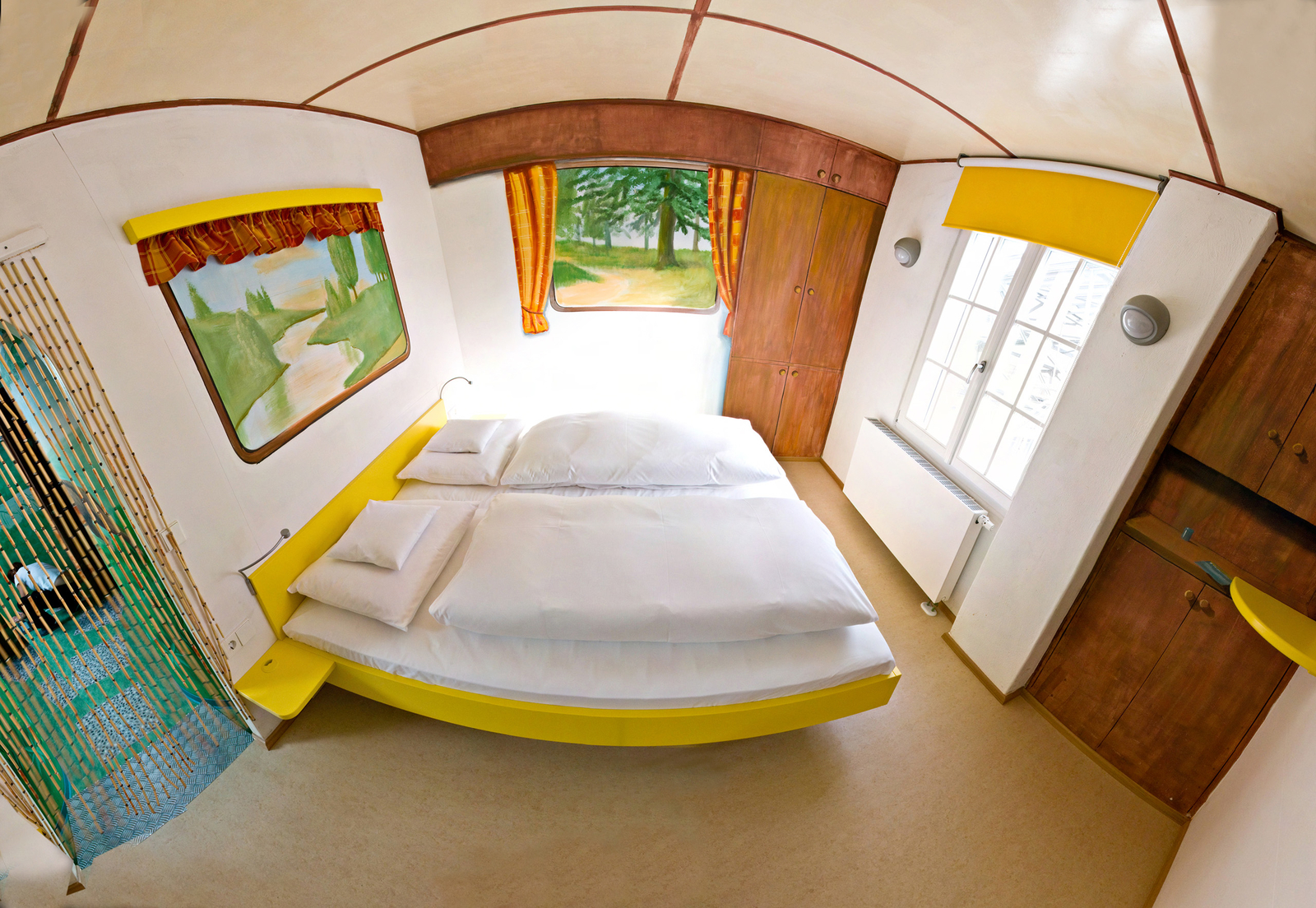 Camping Themenzimmer eingerichtet mit einem gelben Doppelbett und aufgemalten Fenstern, die die Landschaft zeigen