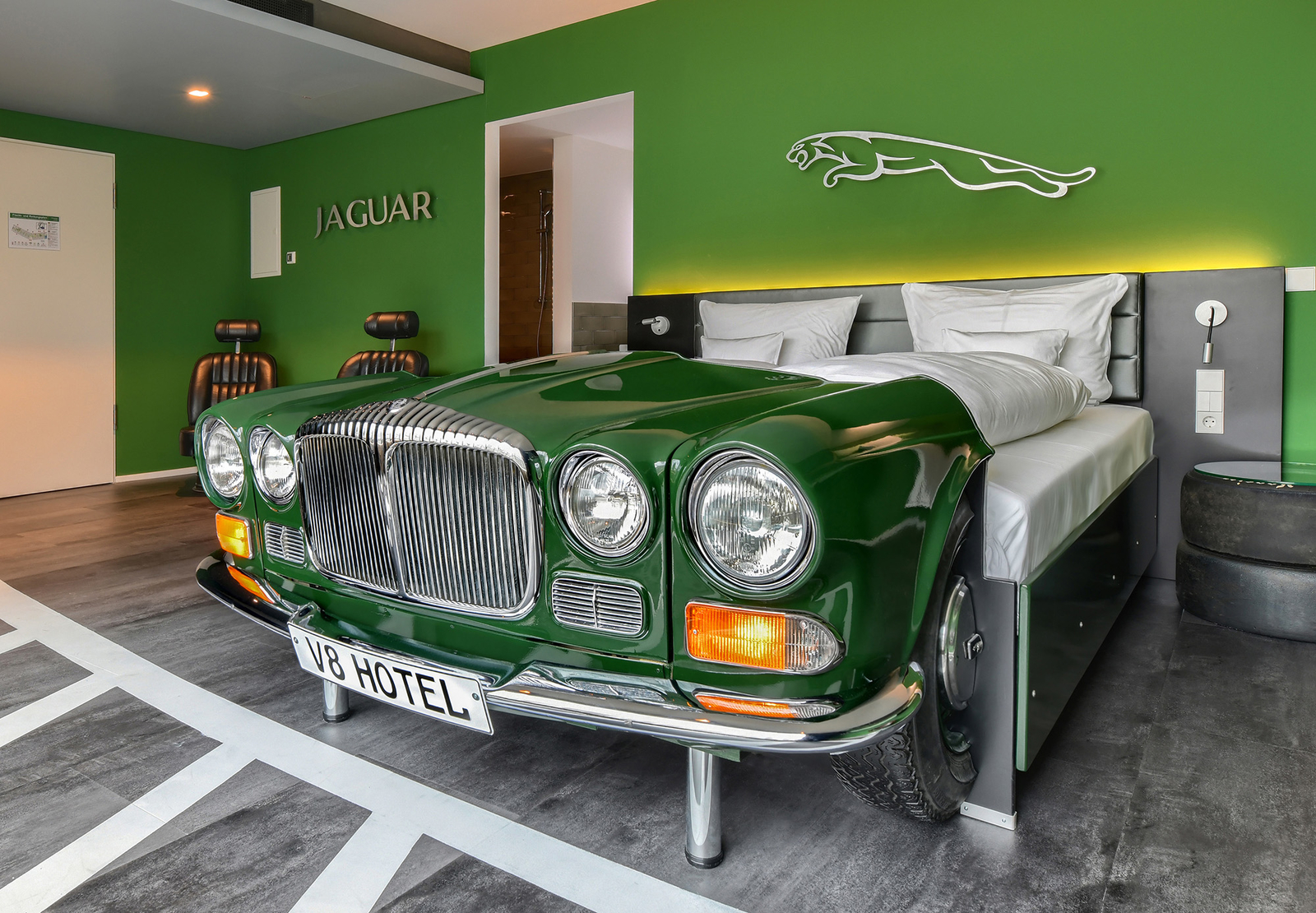 Grünes Autobett im Jaguar-Themenzimmer im V8 Hotel an einer grünen Wand mit silbernem Jaguar-Logo