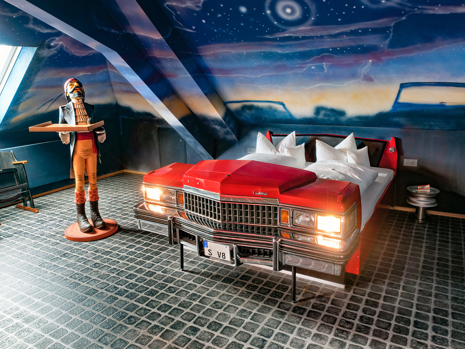 Bett in einem Roten Cadillac an einer Wand bemalt mit einem Sternenhimmel im Autokino-Themenzimmer