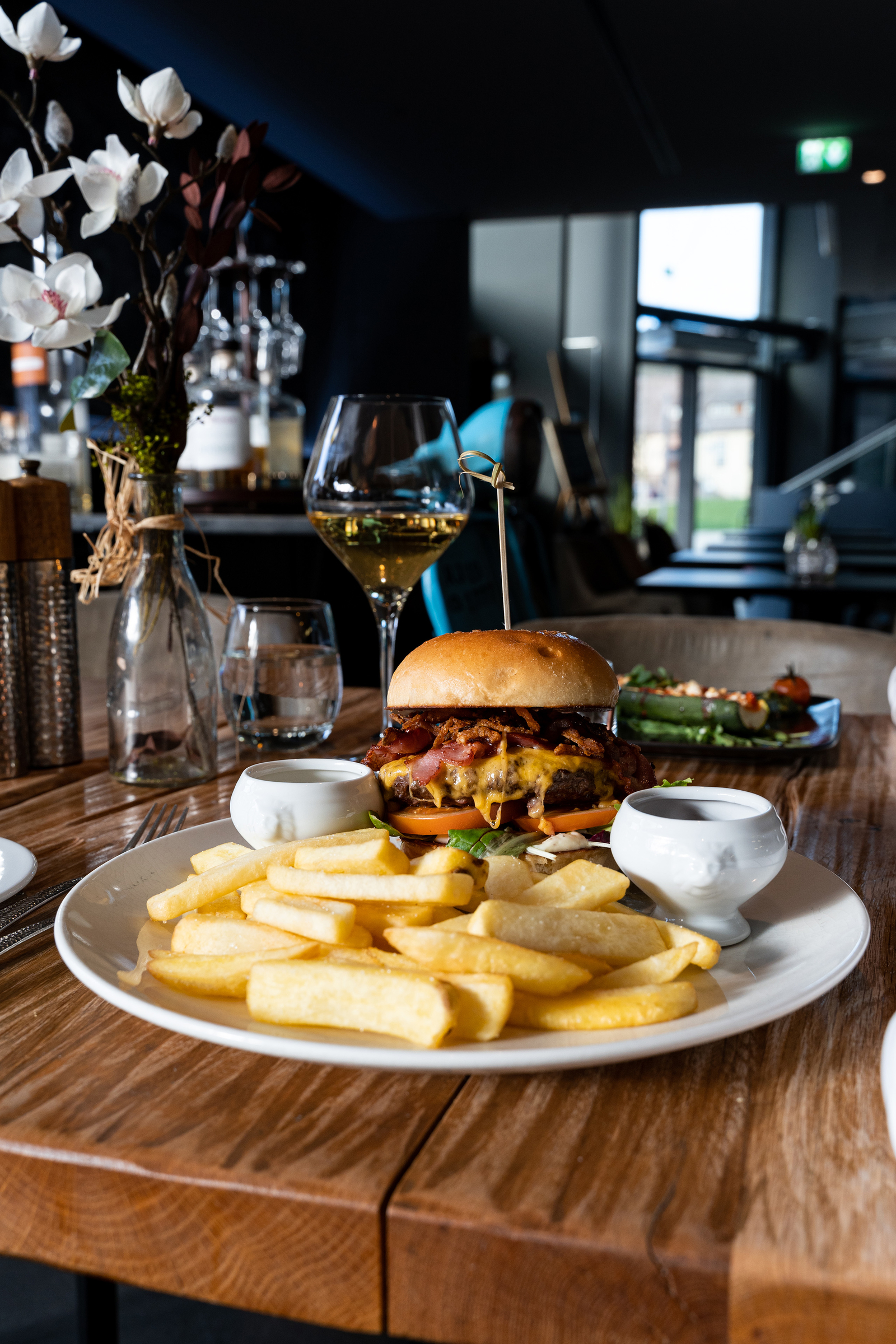 Hausgemachter Burger serviert mit Pommes und einem Weißwein auf einem Holztisch im Restaurant