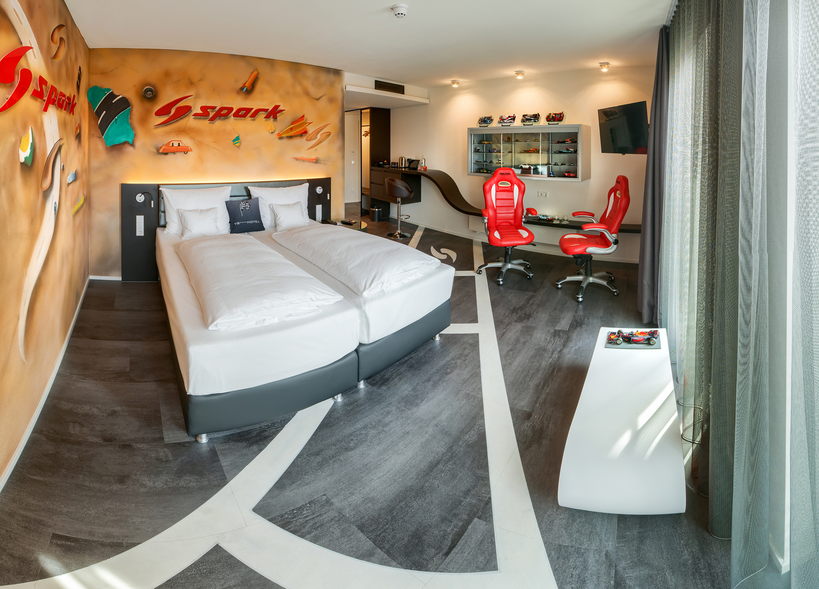Spark-Themenzimmer im V8 Hotel mit passend bemalten Wänden und zwei roten Schreibtischstühlen neben dem gemütlichem Doppelbett