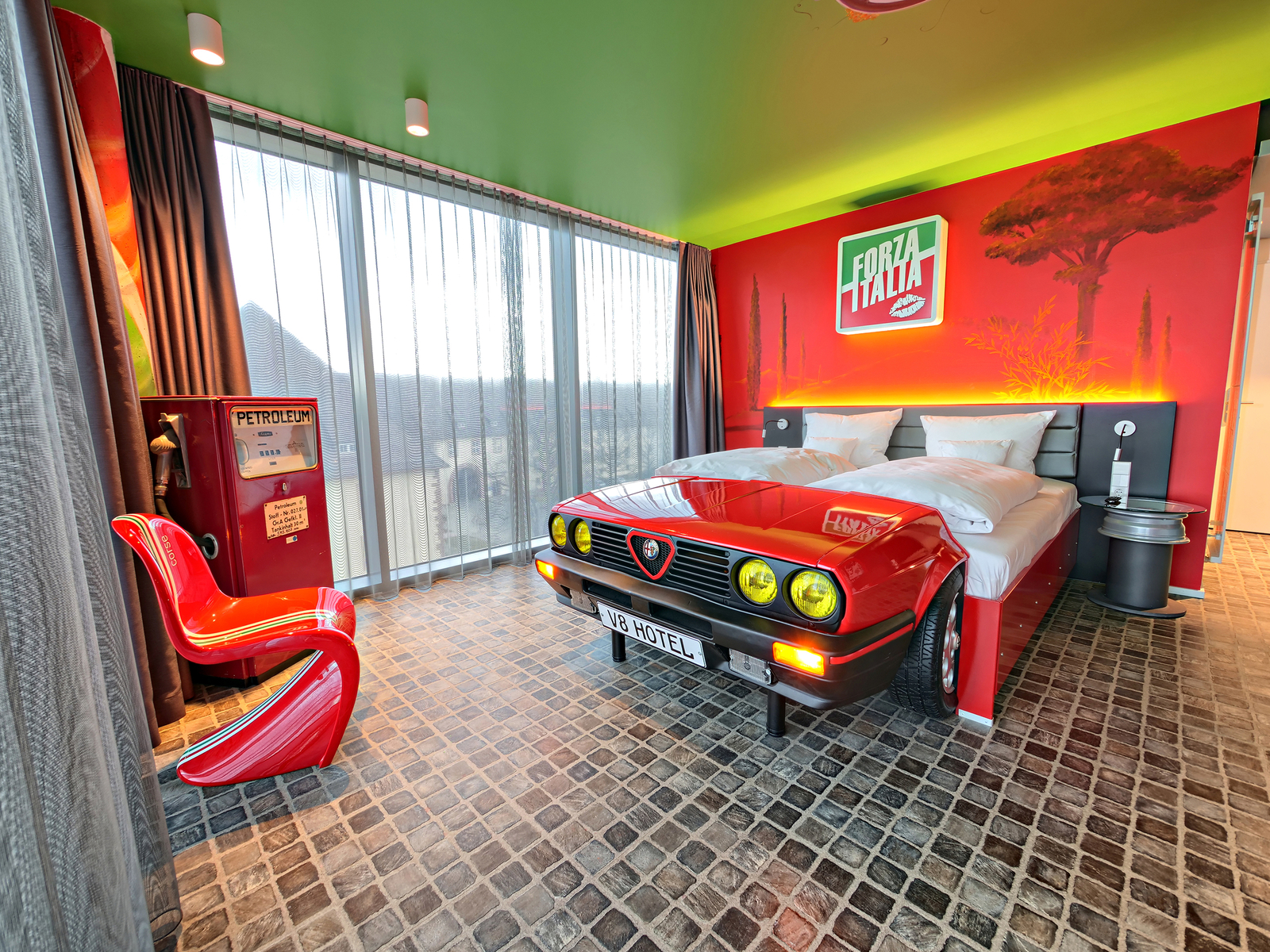 Italia-Themenzimmer im V8 Hotel mit einem roten Autobett neben einer Fensterfront und einer roten Zapfsäule