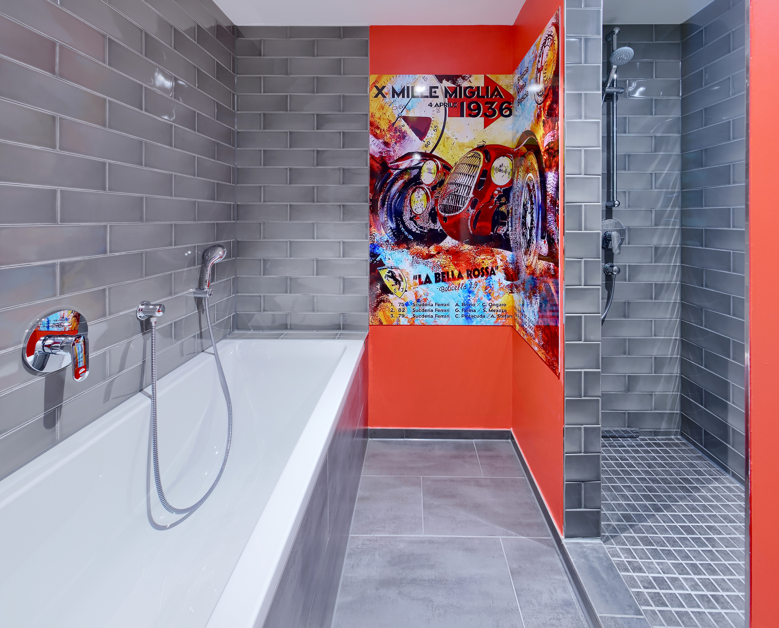 Das Bild zeigt ein modernes Badezimmer mit einer weißen Badewanne auf der linken Seite, grauen Fliesenwänden und einer ebenerdigen Dusche rechts. An einer Wand befindet sich ein farbenfrohes Wandbild, das historische Autos und den Text "X Mille Miglia 1936" zeigt.