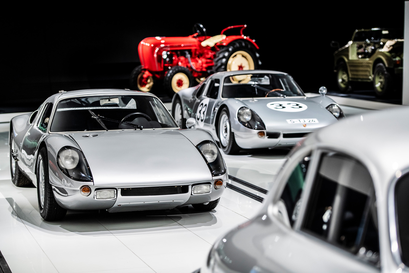 Mehrere silberne, alte Porsches stehen im Porschemuseum, im Hintergrund Traktoren.
