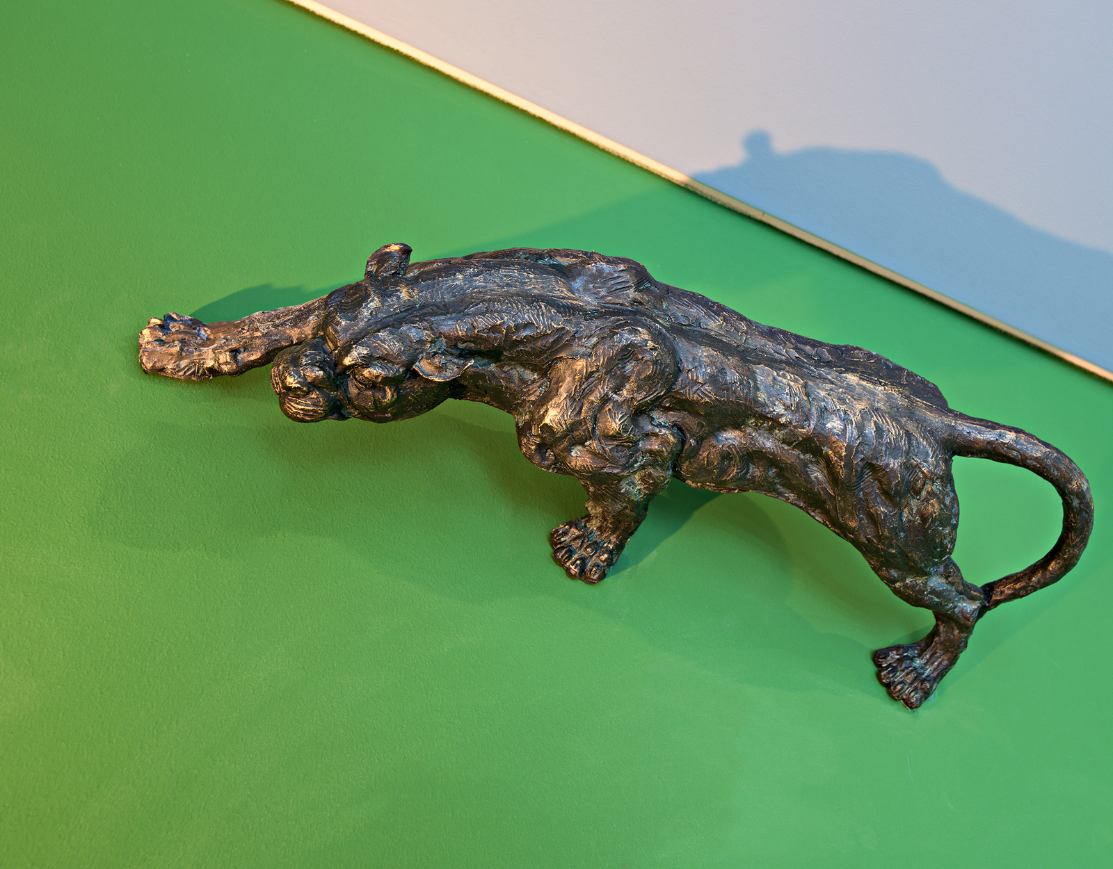 Eine bronzene Skulptur eines Jaguars, das sich vorwärts streckt, mit detaillierten Texturen auf dem Körper. Die Statue befindet sich auf einem grünen Hintergrund, der die Konturen des Tieres betont.