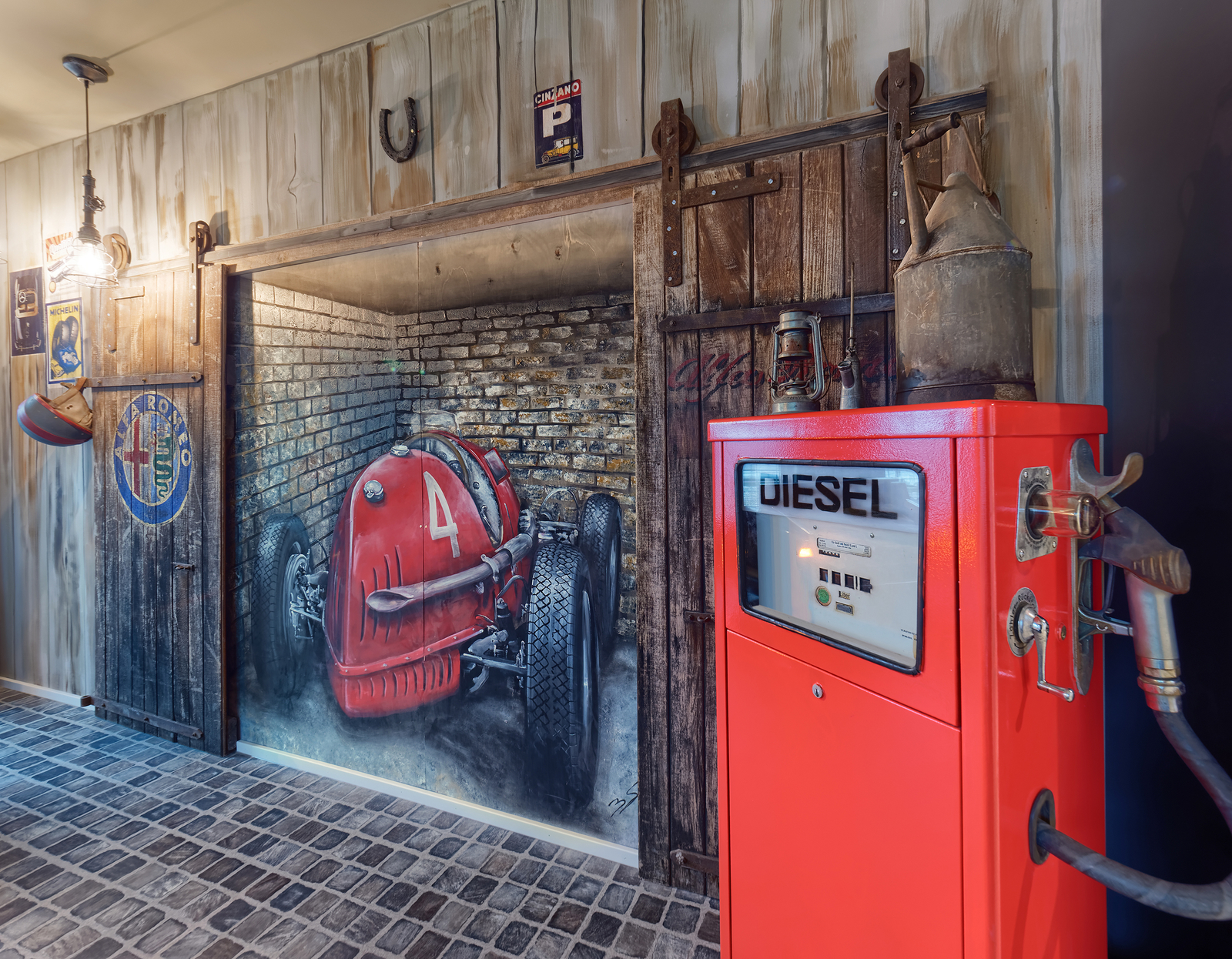 Wand des Scheunenfund-Autozimmers mit Rennauto in einer Scheune sowie einer roten Diesel-Zapfsäule im Vordergrund.