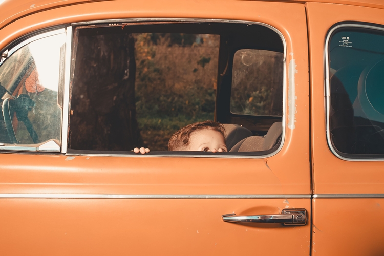 Ein Kind blickt aus dem Fenster eines orangefarbenen vintage Autos