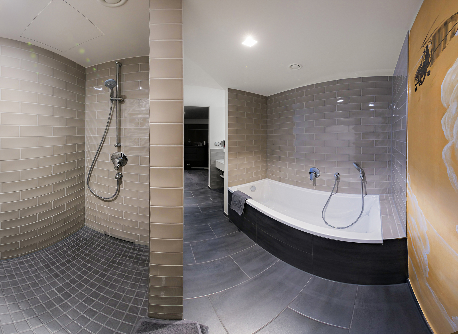 Das Bild zeigt ein modernes Badezimmer mit einer Dusche in einer Ecke und einer freistehenden Badewanne. Die Wände sind mit hellen Fliesen gefliest, und der Boden ist in einem dunkleren Farbton gehalten. Es gibt eine große Spiegeloberfläche und elegante Armaturen.