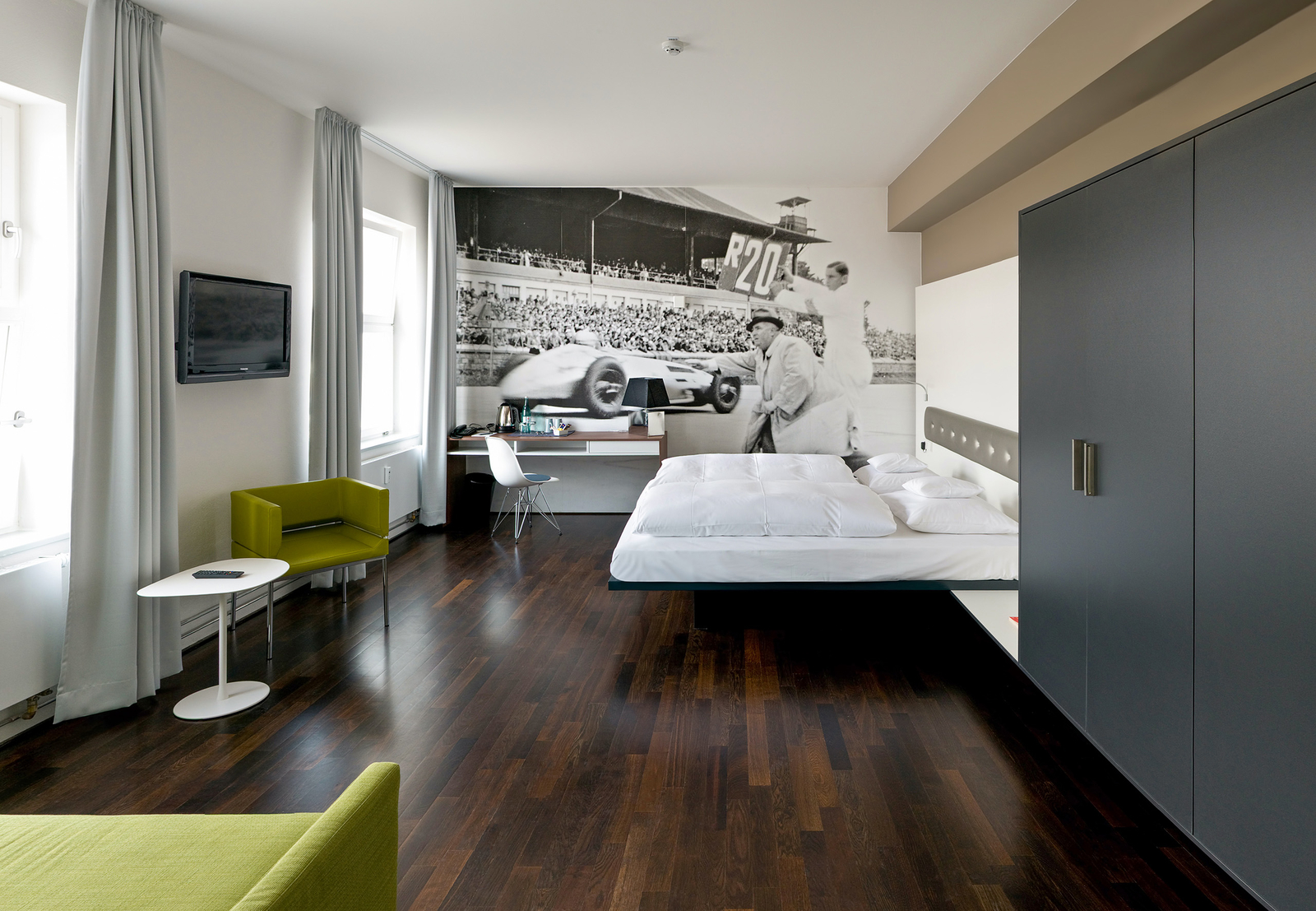 Großzügiges Schlafzimmer mit Doppelbett, zwei grünen Sessel und einem Schreibtisch an einer Wand mit schwarz-weiß Motivtapete 