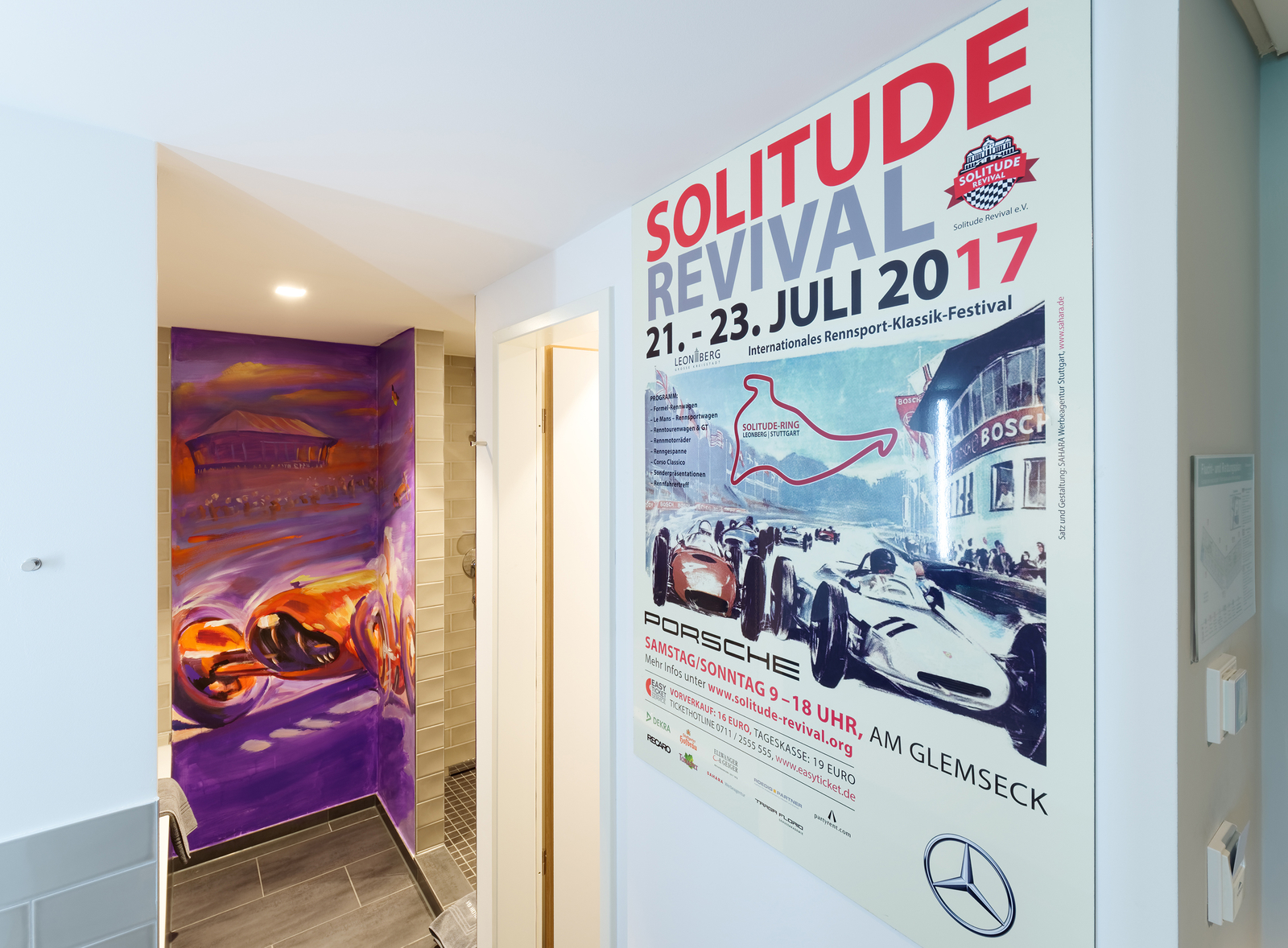 Ein buntes Wandbild und ein Plakat für das "Solitude Revival" Festival, das vom 21. bis 23. Juli 2017 in Leonberg stattfindet. Das Plakat zeigt Rennwagen und das Logo von Mercedes und Porsche, sowie eine Karte des Solitude-Rings.