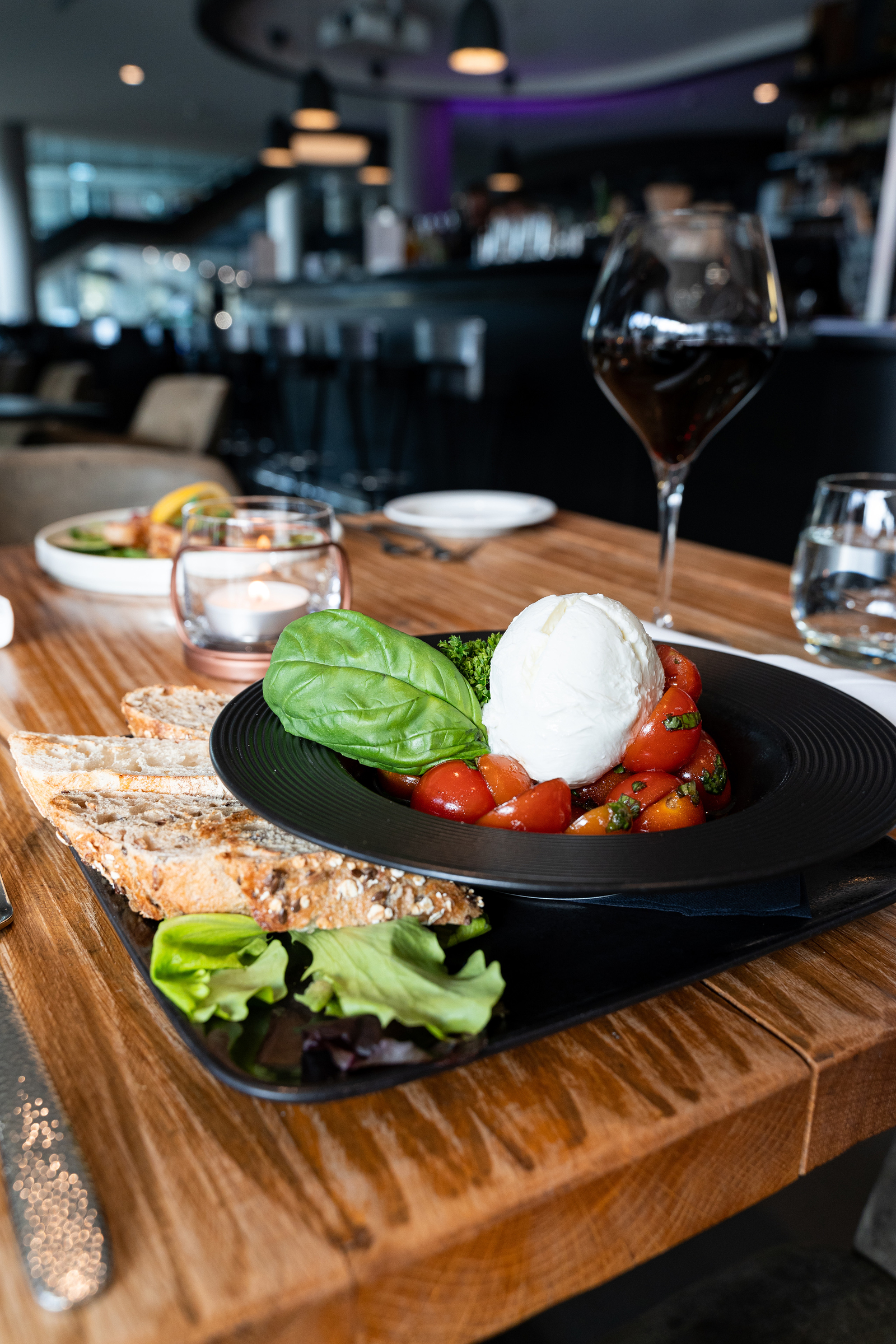 Burrata auf Tomaten mit Basilikum serviert mit Brot und einem Glas Rotwein