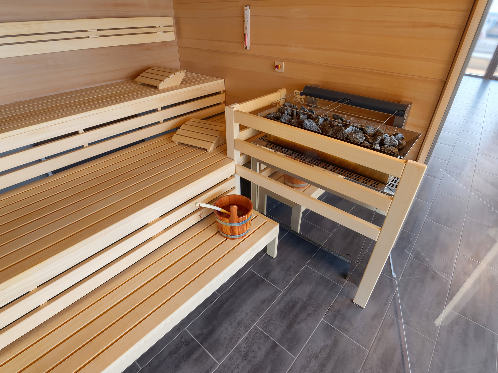 Blick auf zwei Liegestühle im Wellnessbereich des Hotels mit großer Holzsauna im Hintergrund.