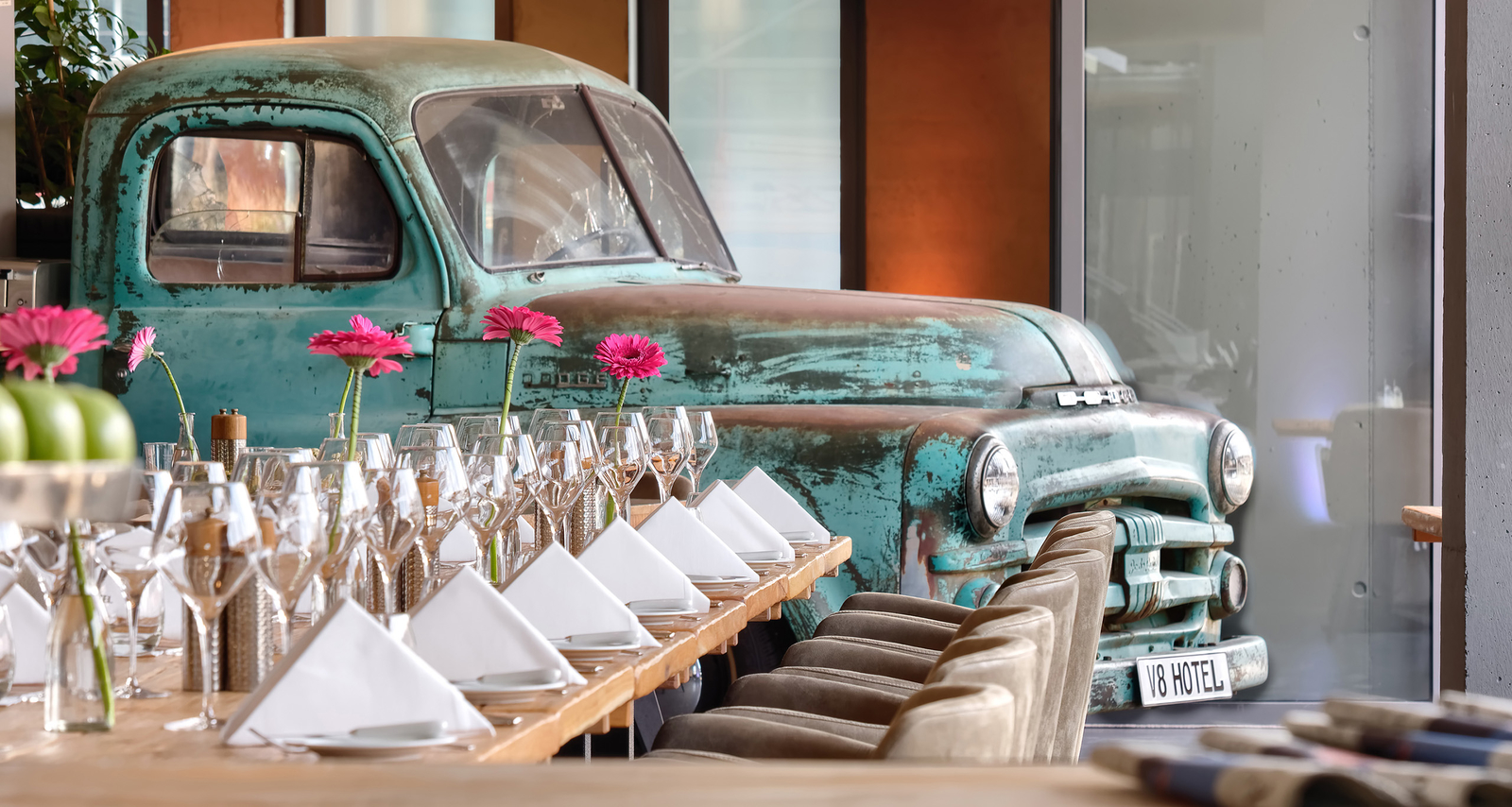 Lange gedeckte Tafel dekoriert mit pinkfarbenen Blumen vor einem hellblauen Pick-Up