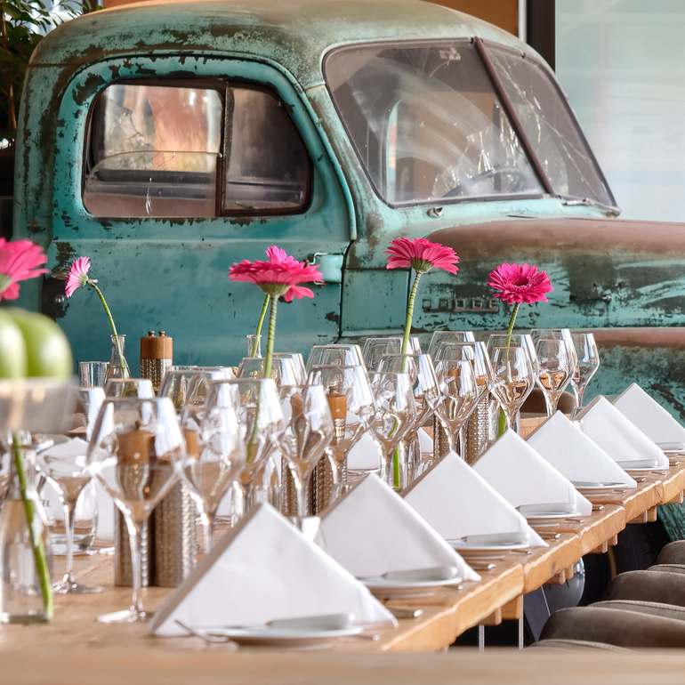 Alter hellblauer Pick-Up hinter einer langen Tafel dekoriert mit pinken Blumen