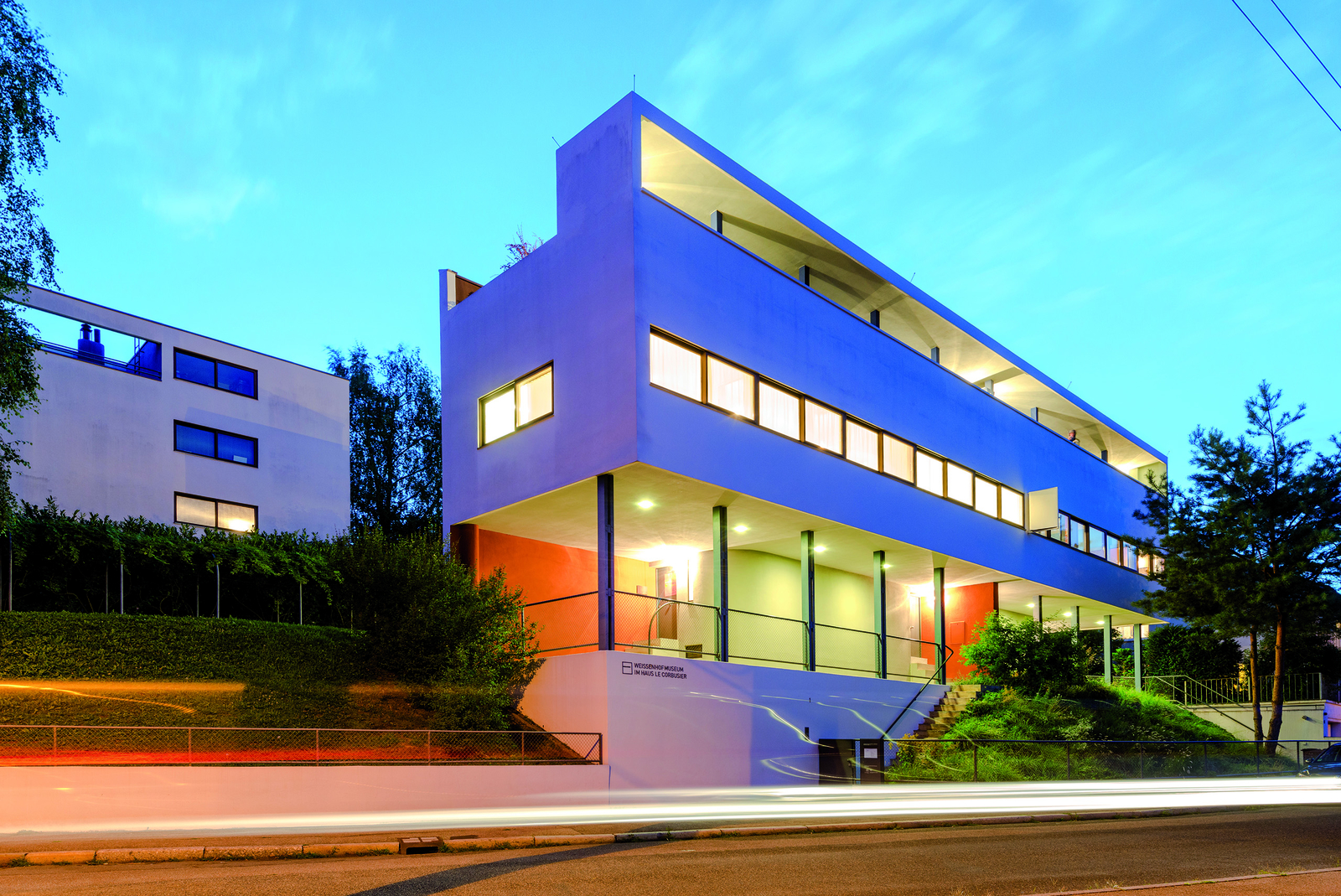 Blick von außen auf das moderne, weiße und beleuchtete Gebäude des Weissenhofmuseums bei Dämmerung.