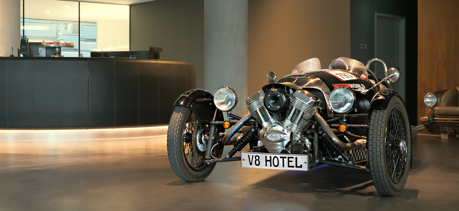 Ein schwarzes, altes Motorrad steht im Eingangsbereich des Hotels mit Kennzeichen "V8 Hotel".