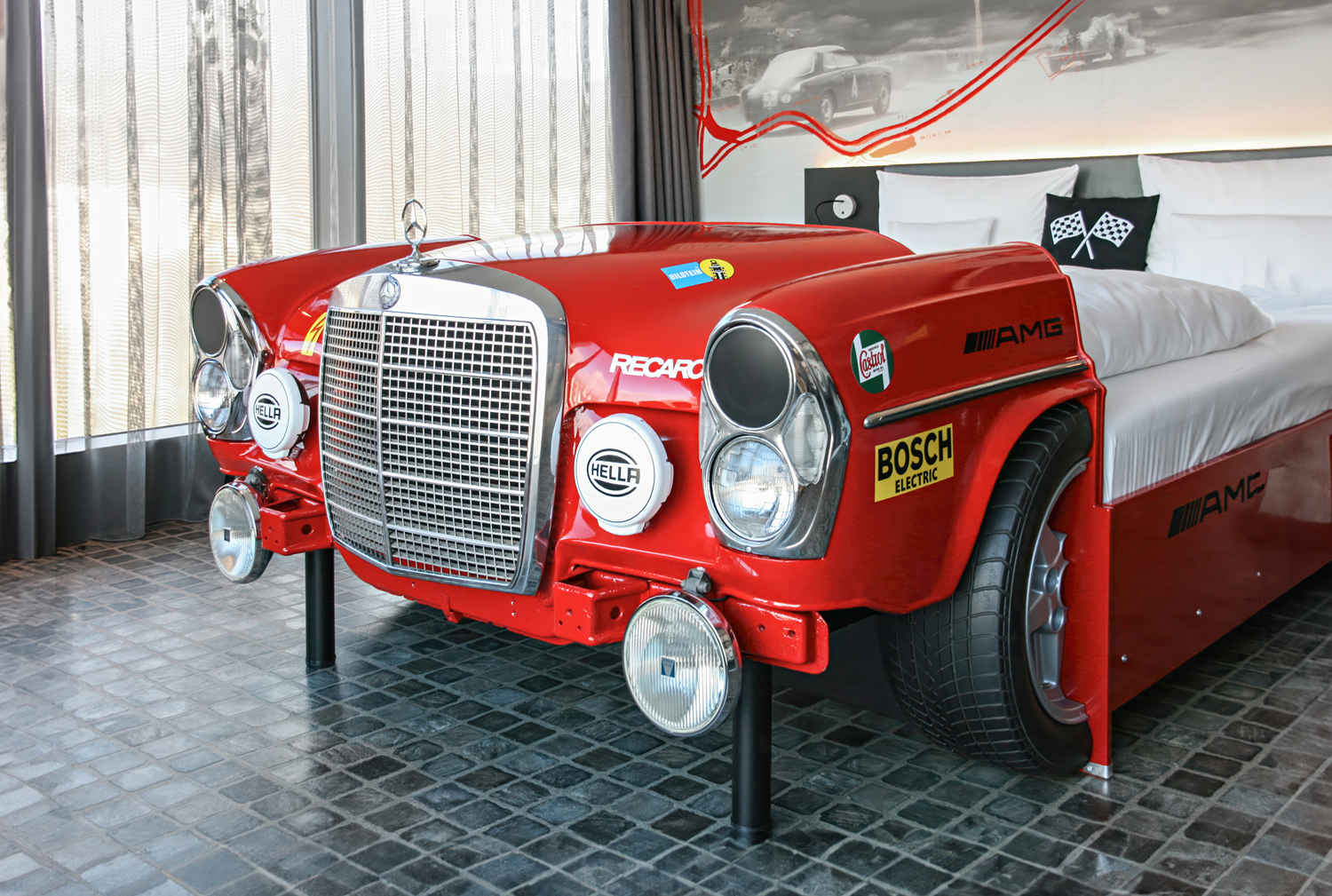 Autozimmer Solitude Revival mit Mercedes-Autobett und schwarz-weißen themenbezogenen Motivtapeten mit Oldtimern.