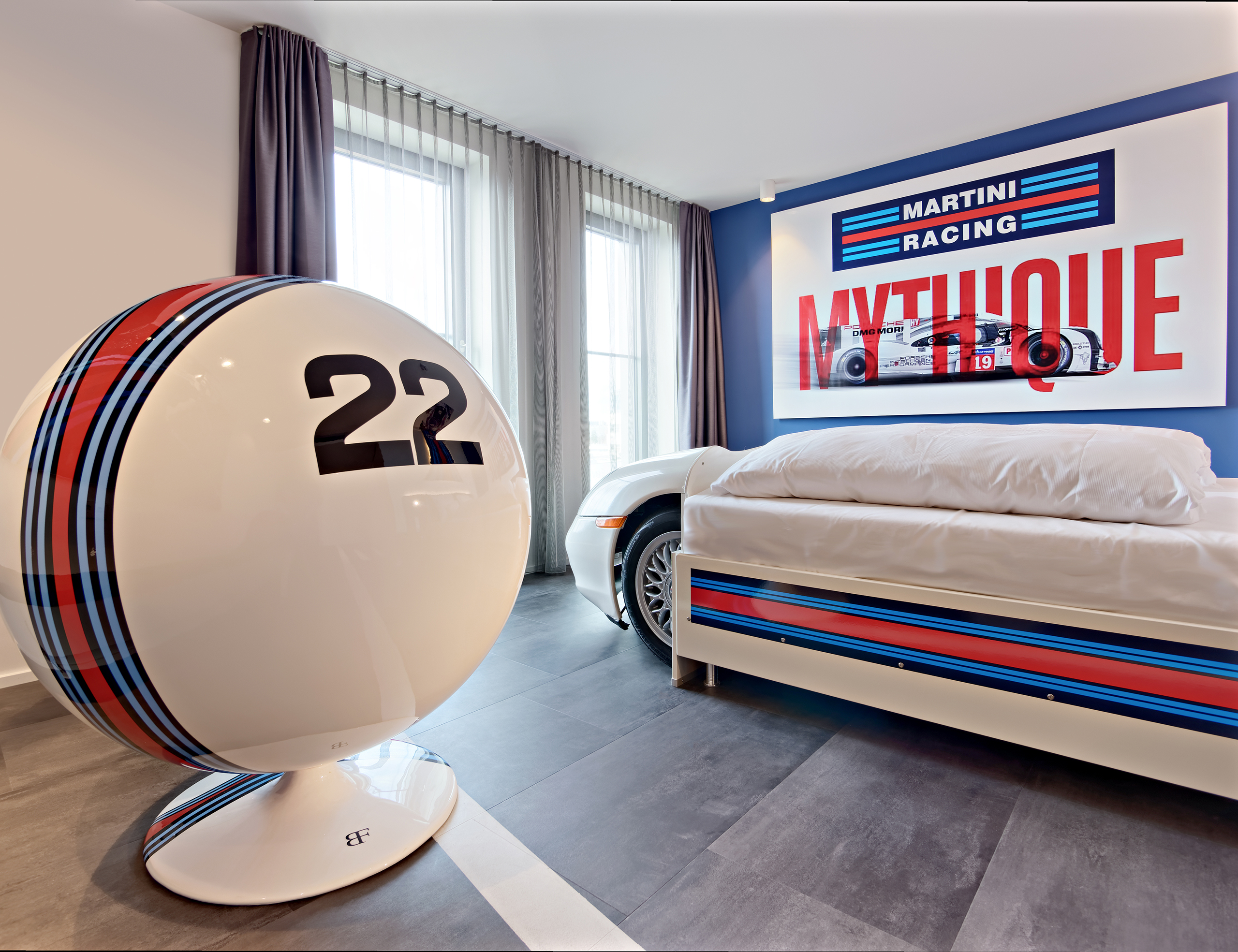 Autozimmer Petrol Heads mit weißem Autobett, Martini Racing Logos an den Wänden und dem Bett sowie ein großer Sessel.